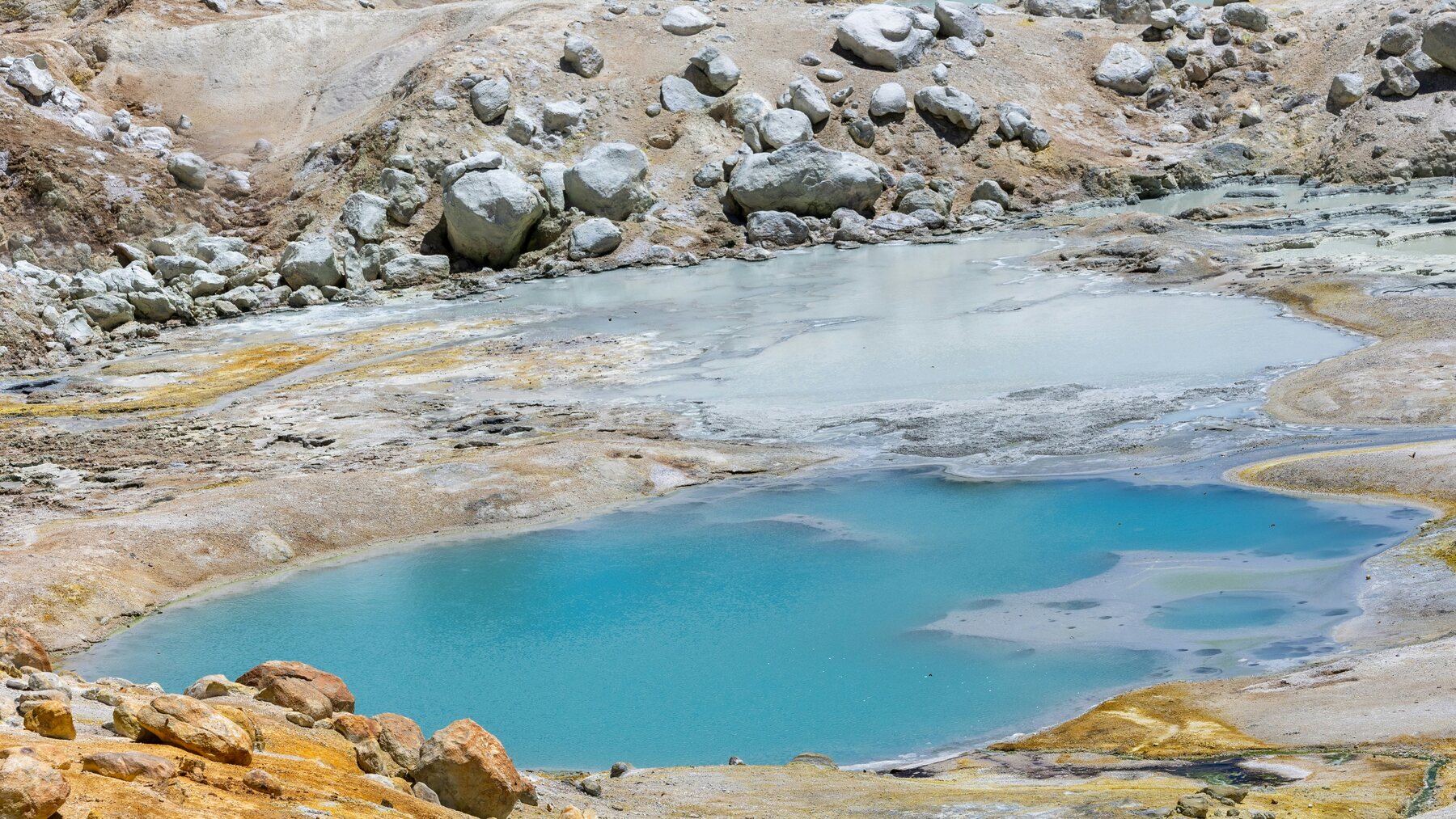 Blue geothermal pool surrounded by steaming mineral-covered rock at Lassen Volcanic National Park