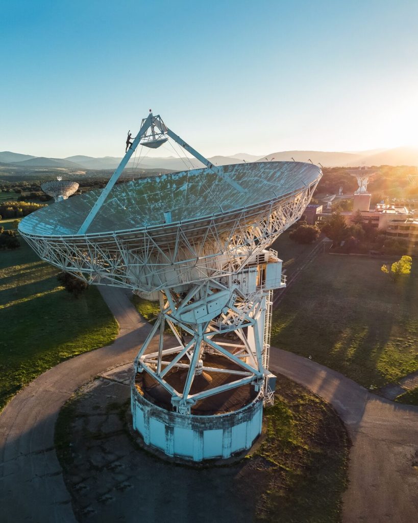 Aerial view of a large satellite dish at sunset with mountains behind it