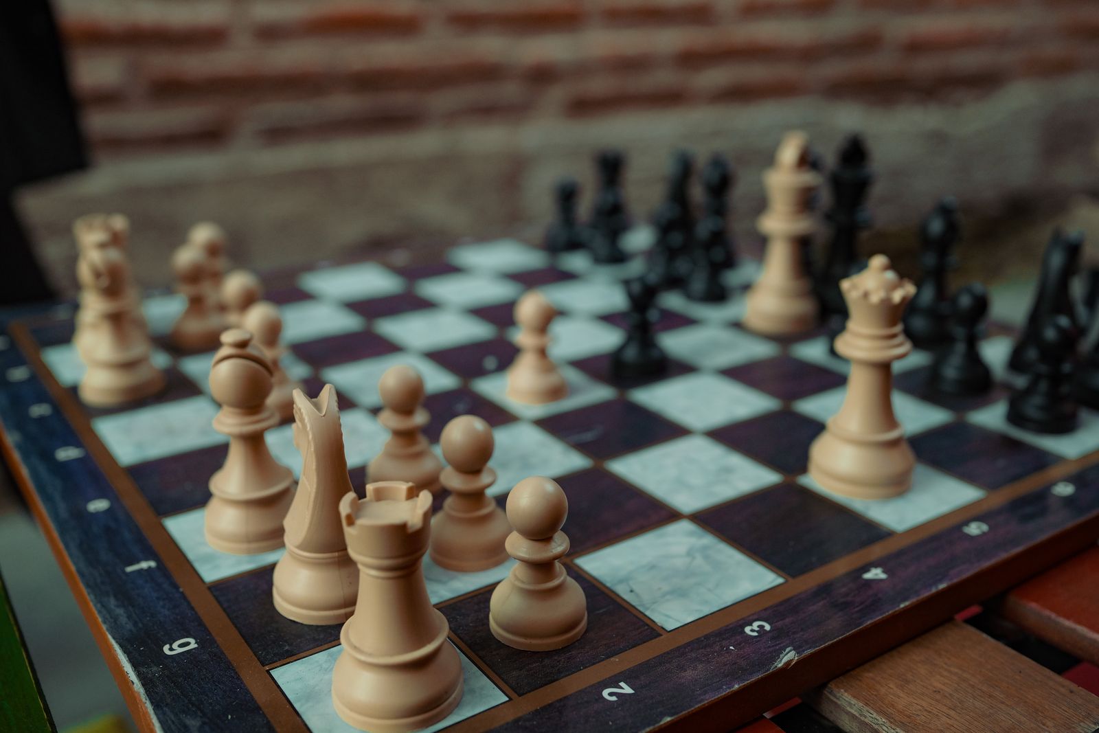 Wooden light and dark chess pieces arranged on a checkered board on a table.