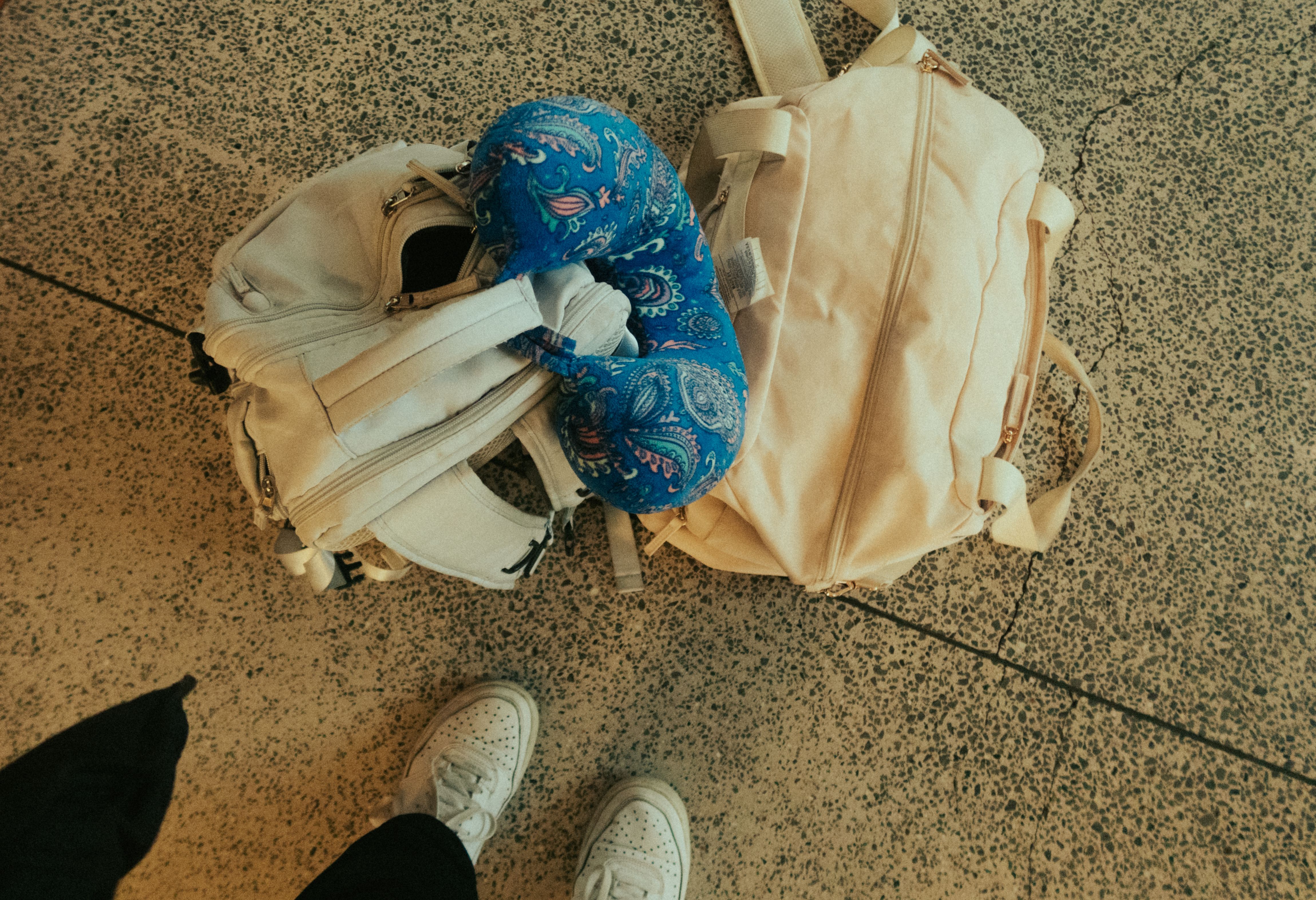Black travel bag, backpack, suitcase and neck pillow arranged on an airport floor.