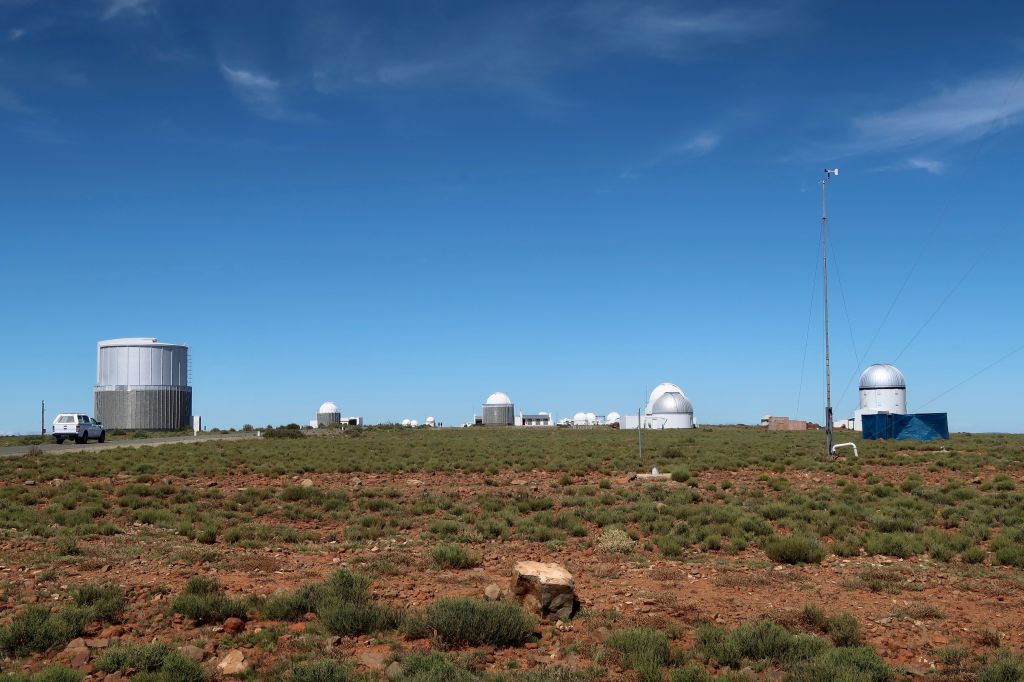 Astronomical observatory domes in a dry open landscape beneath a clear blue sky.