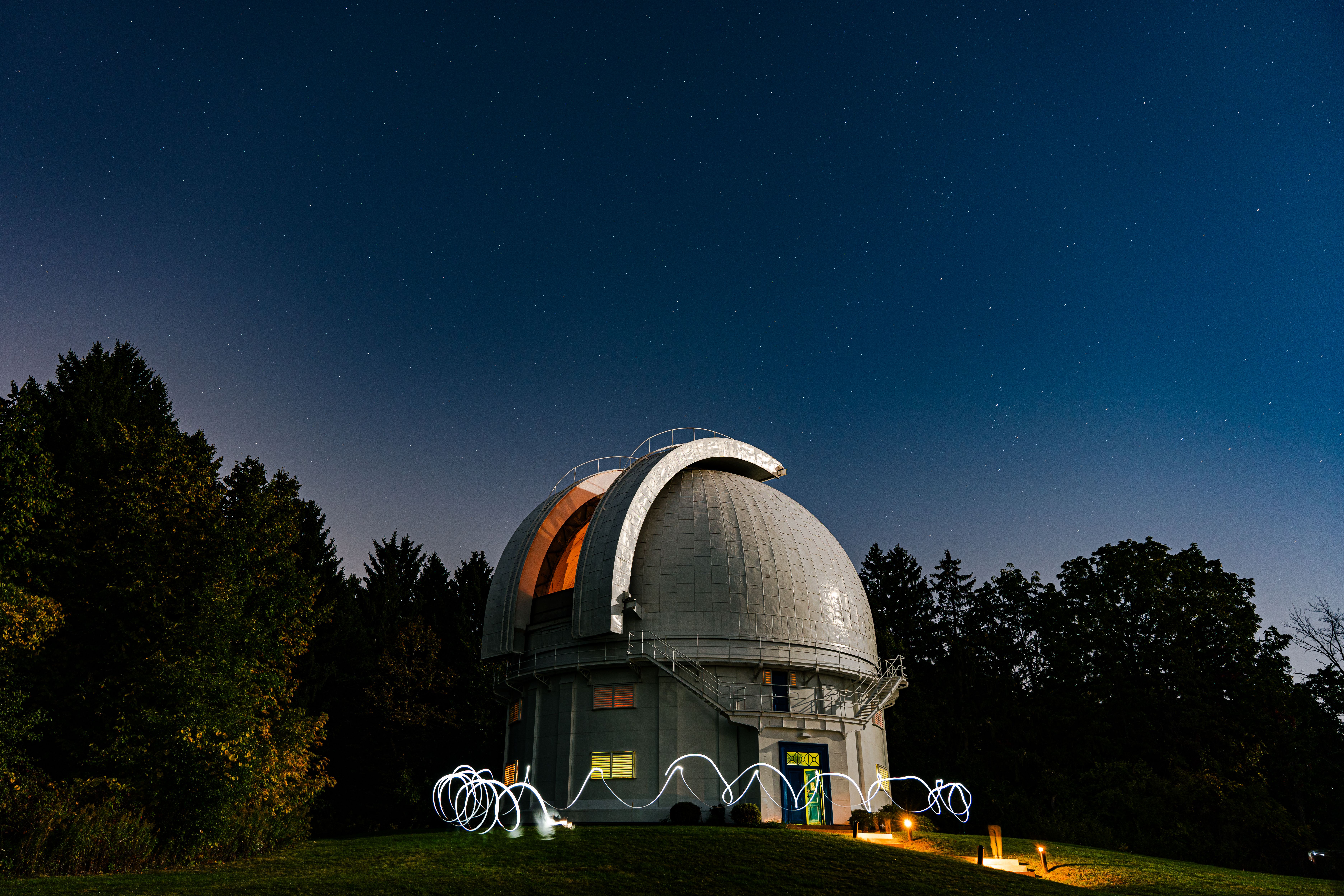 Observatory dome beneath a star-filled night sky, surrounded by trees.