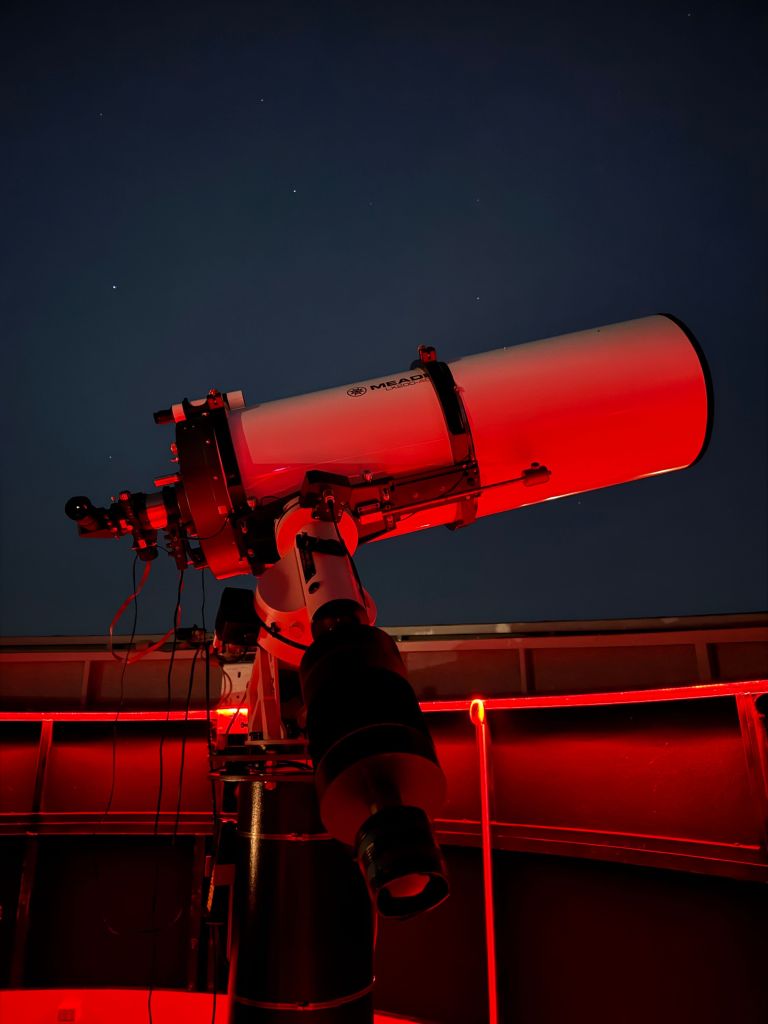 Large telescope inside a red-lit observatory pointing through an open dome.