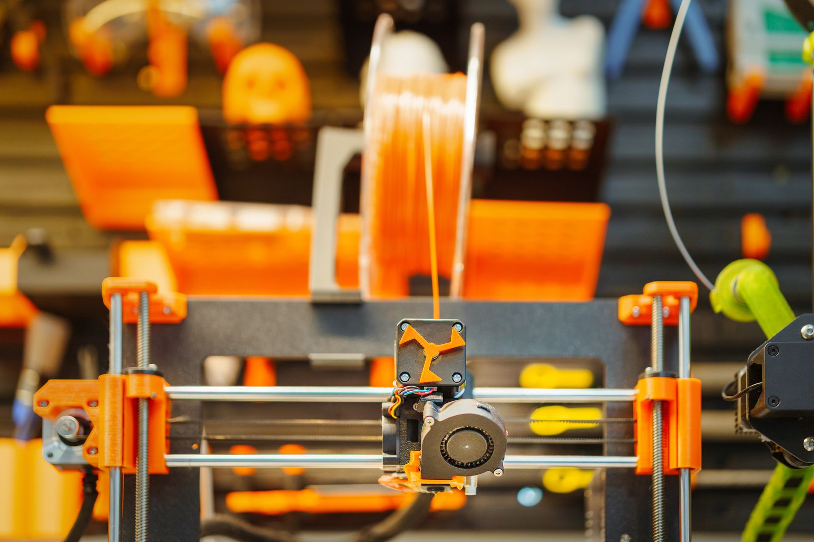 Close-up of a black and orange desktop 3D printer toolhead positioned above a textured build plate.